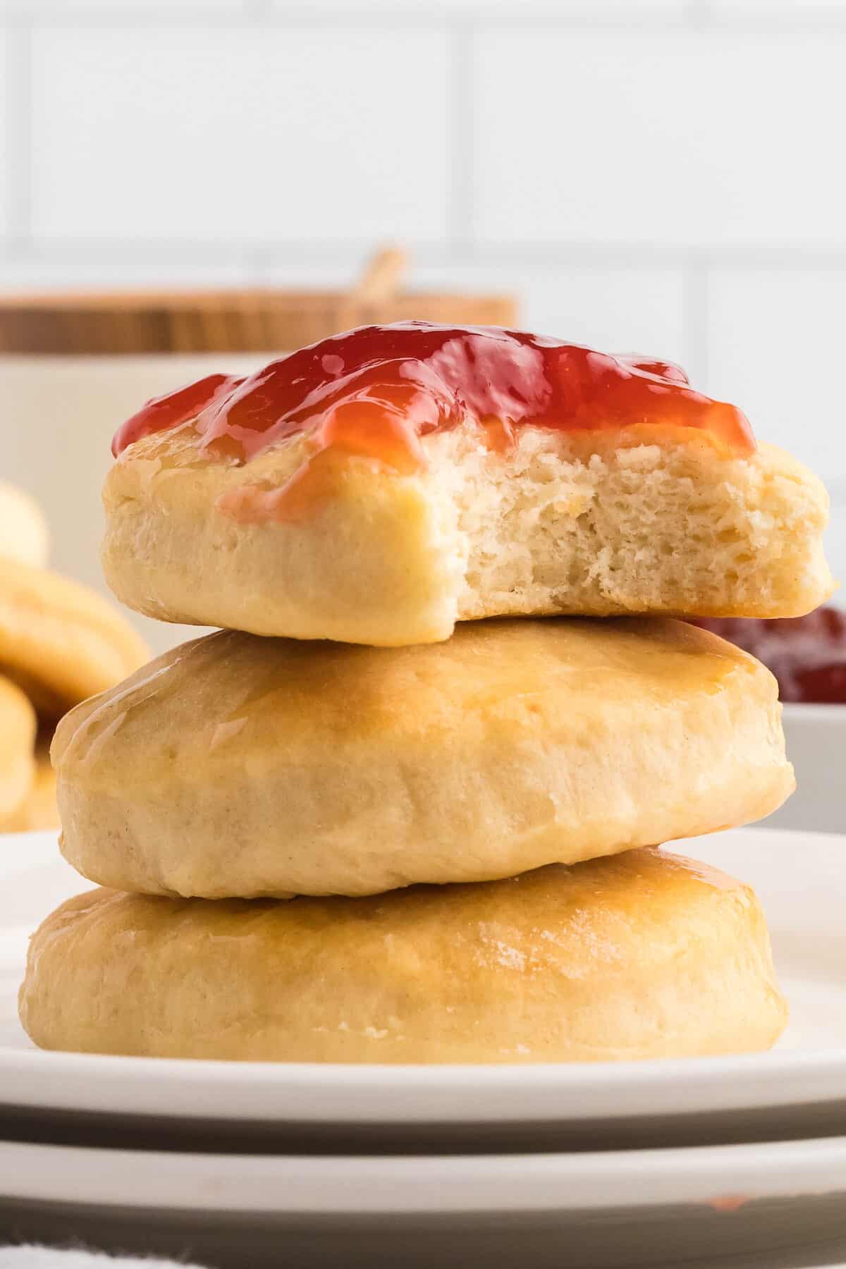 stack of three honey butter scones with strawberry jam spread on top with a bite taken out of it.