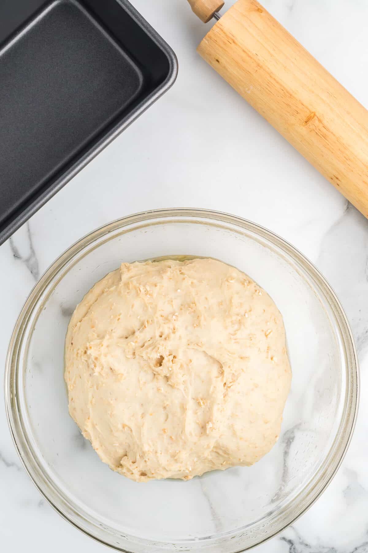 bread dough in the large bowl with a bread pan and rolling pin to the side. 