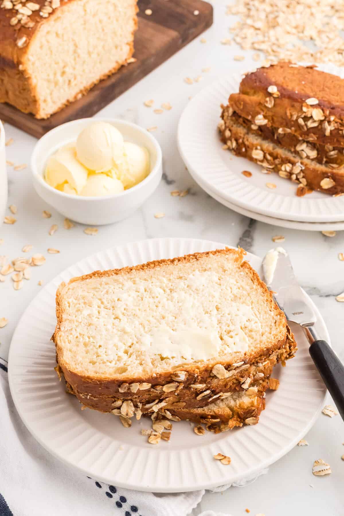 honey oat bread slices on a white plate with butter in a small white bowl to the side. 