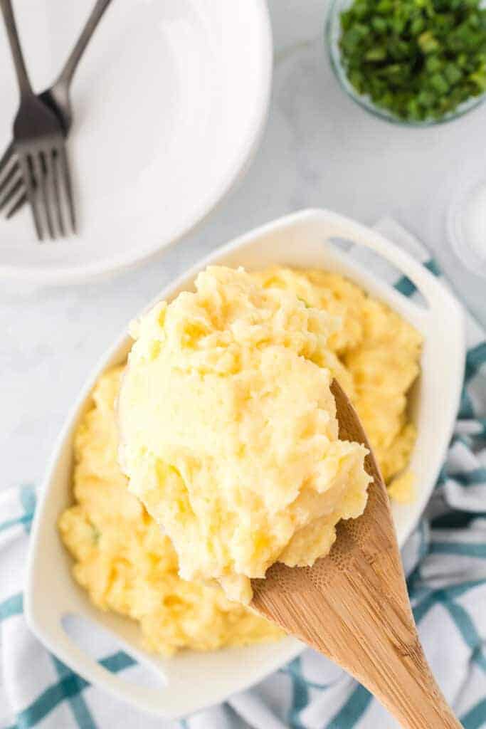 adding the finished ninja foodi mashed potatoes to a serving bowl with a wooden spoon