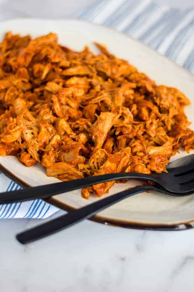 shredded bbq chicken on a white platter with black serving utensils