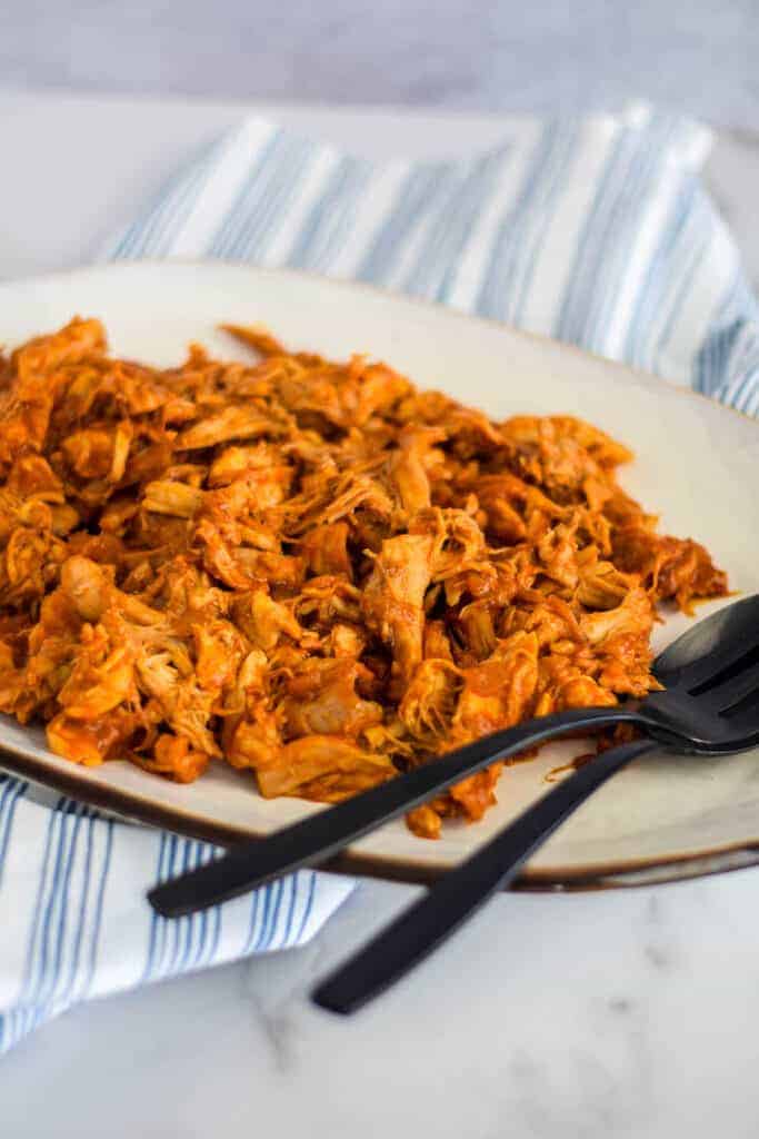 easy shredded chicken with bbq sauce on a white platter with black serving utensils