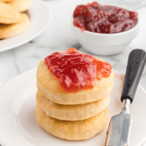 stack of three honey butter scones with strawberry jam spread on top.