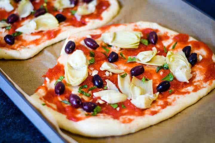 layering of toppings for the olive and artichoke pizza