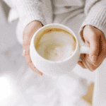lady in neutral sweater with a white cup of homemade latte