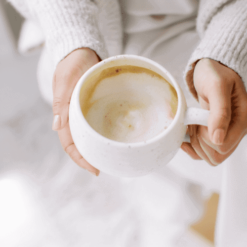 lady in neutral sweater with a white cup of homemade latte