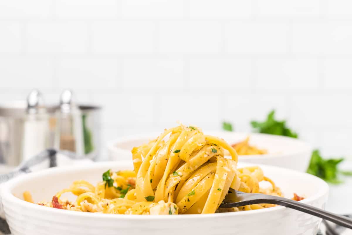 white bowl of chicken carbonara with the pasta twirled around a black fork