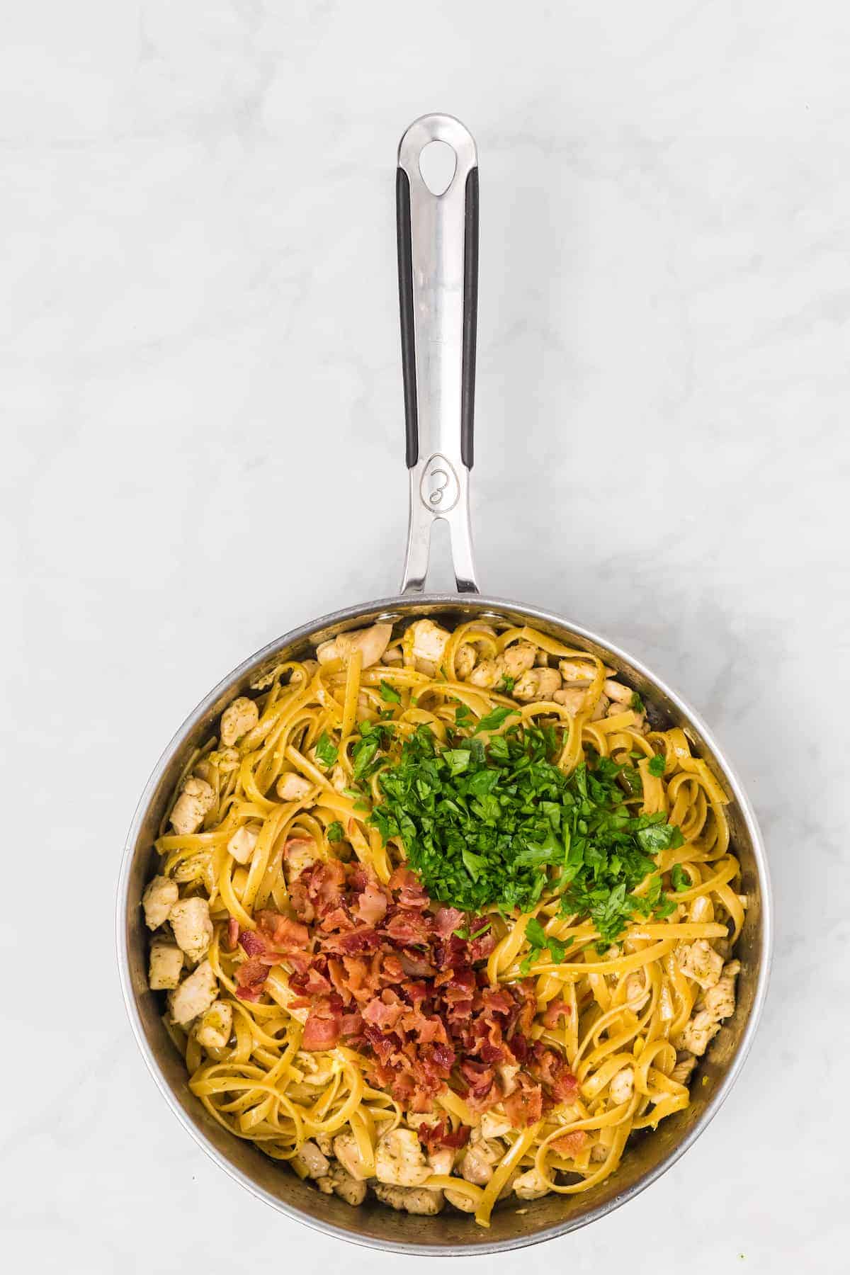 bacon and fresh parsley added to the cooked pasta in the skillet