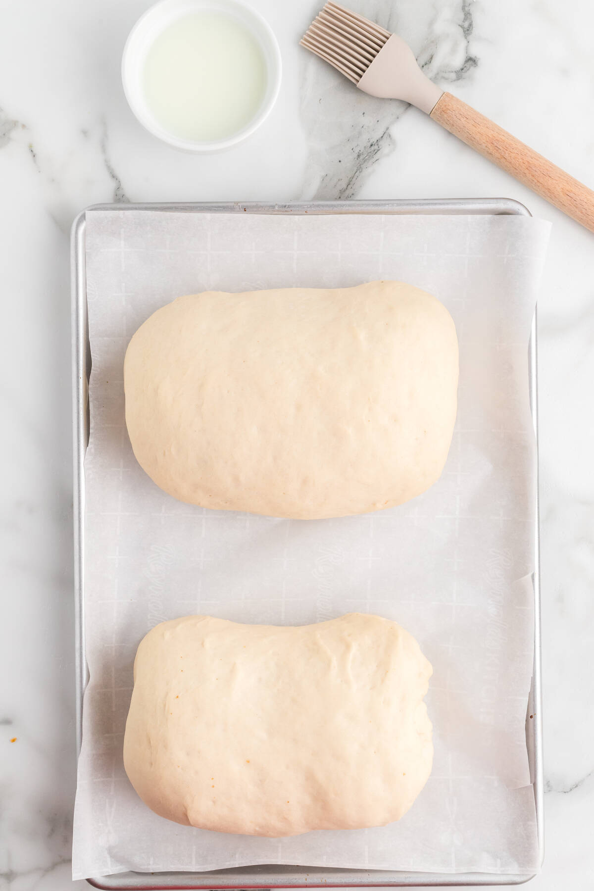 two rustic italian loaves moved to a sheet pan with parchment paper.