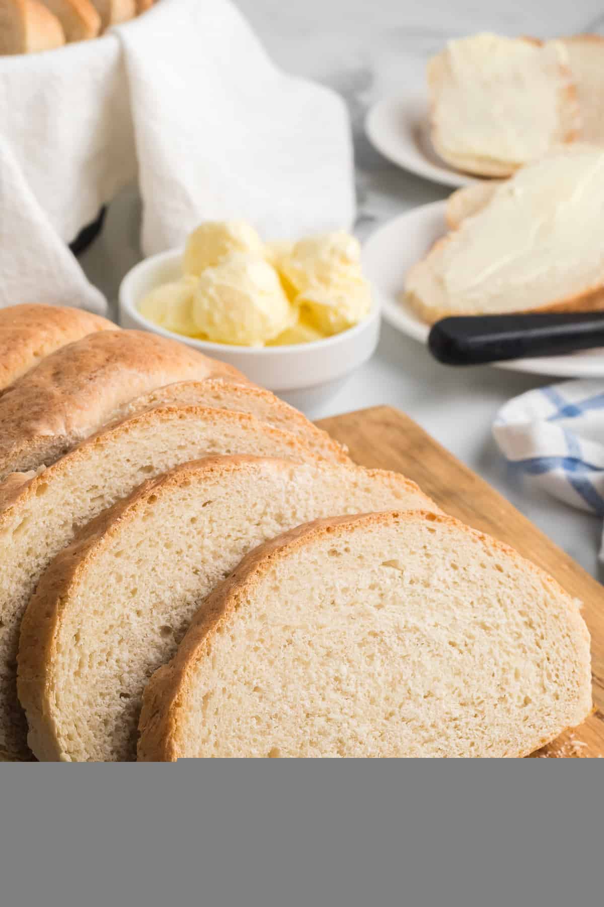 slices of italian loaf bread on a wooden cutting board with a white bowl of butter and knife to the side.