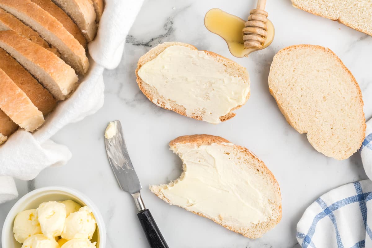 slices of the rustic italian bread loaf spread with softened butter and honey drizzled to the side.