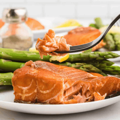 flaky salmon on a white plate with asparagus spears on the backside of the plate.