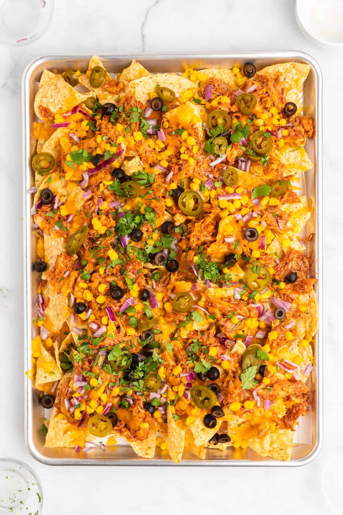 all the toppings layered over top of tortilla chips on a baking sheet. 