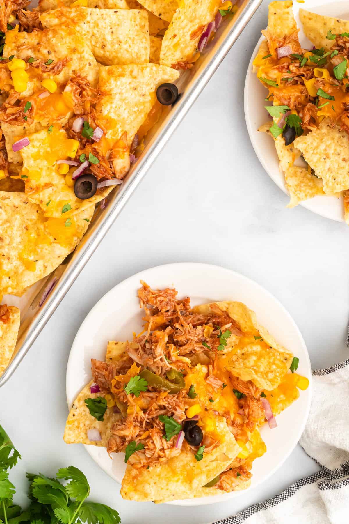 baking sheet with finished bbq chicken nachos and two white plates of nachos