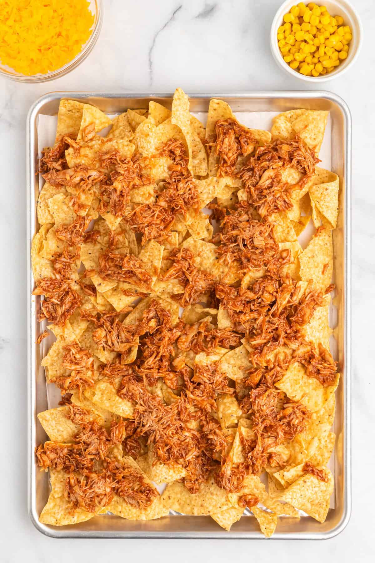 baking sheet with parchment paper, and shredded bbq chicken over tortilla chips. 