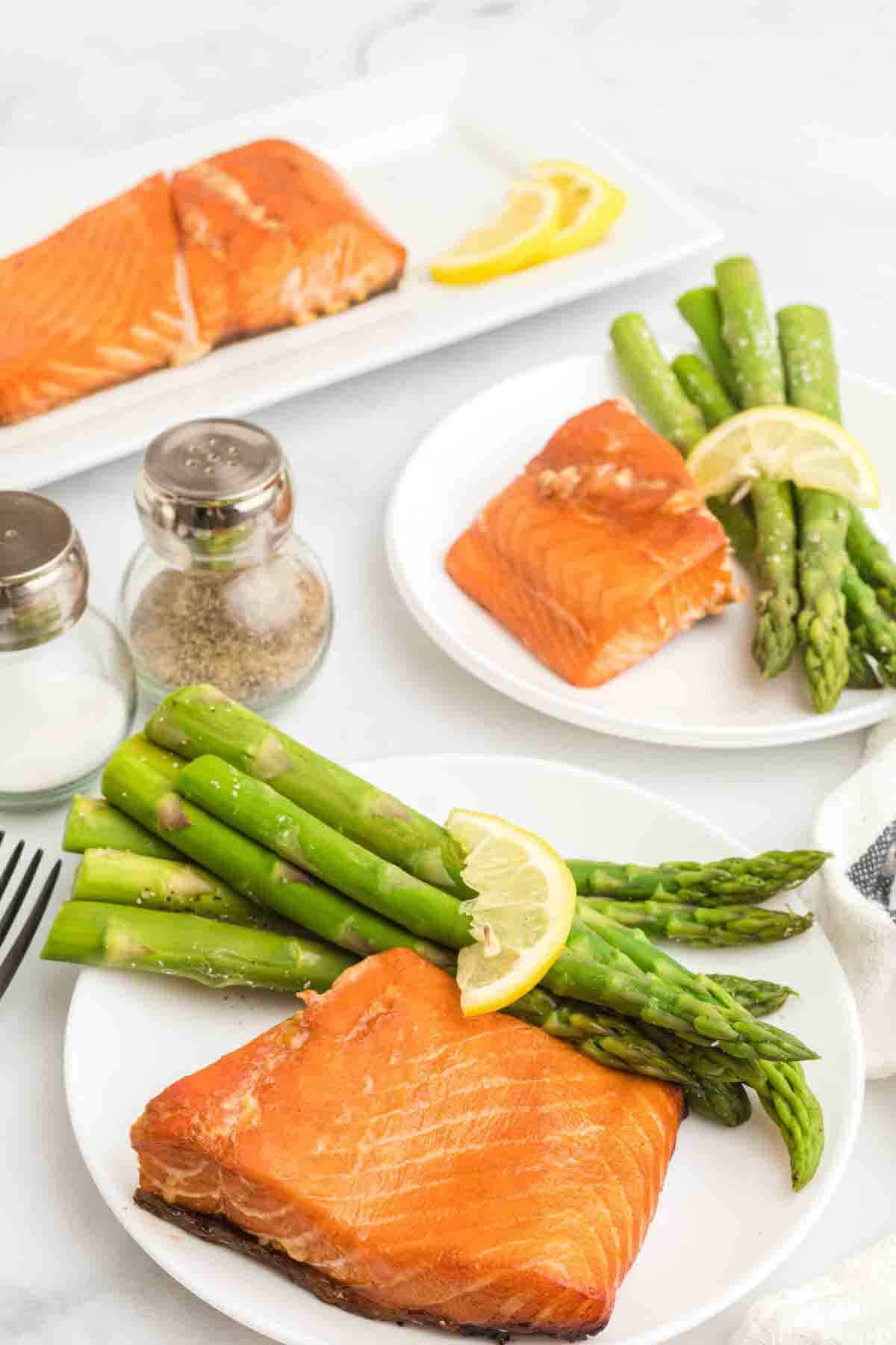 two white plates of Traeger salmon with asparagus and lemon wedges on top.