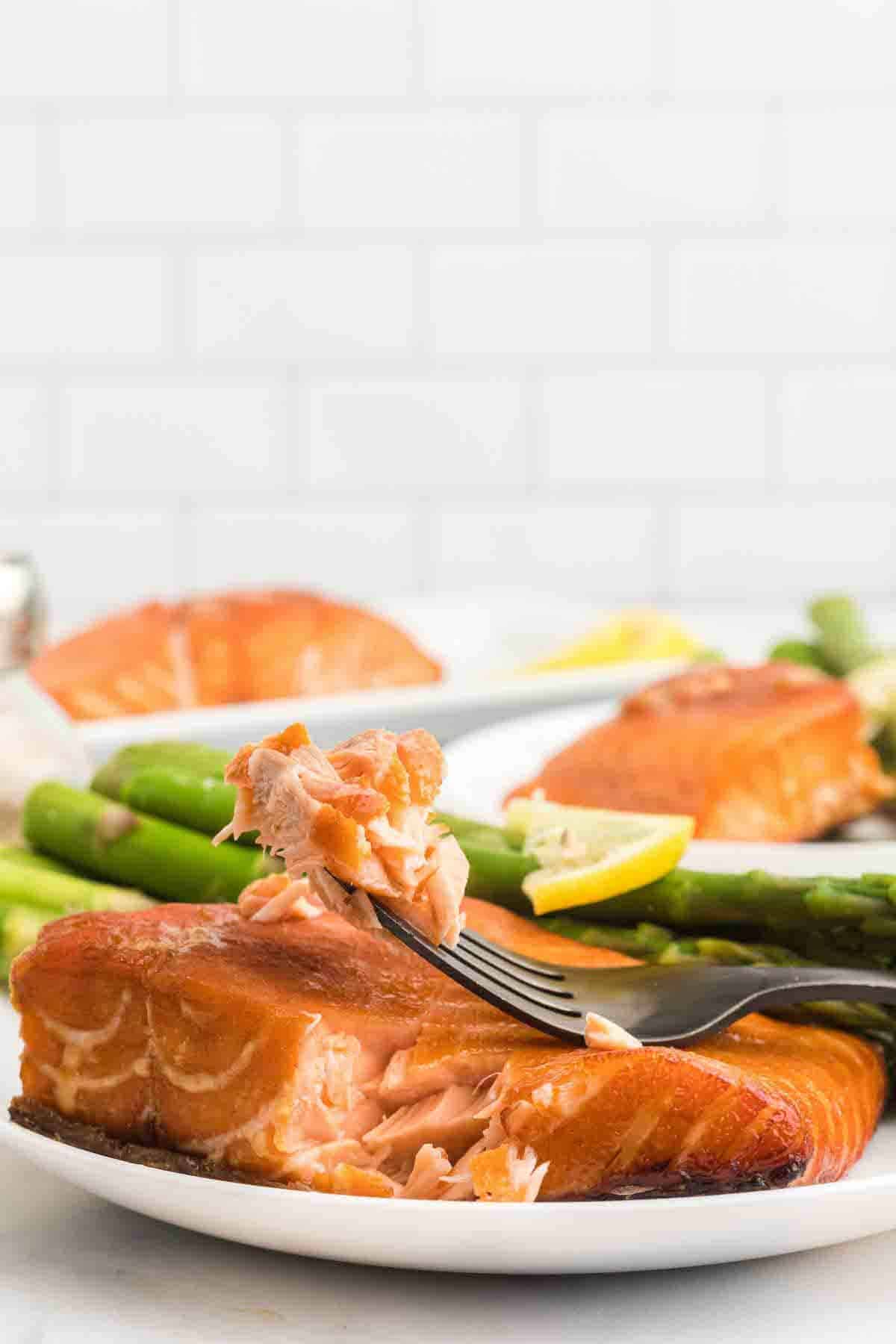 black fork with flaky salmon pieces on it resting above the salmon fillet on a white plate.