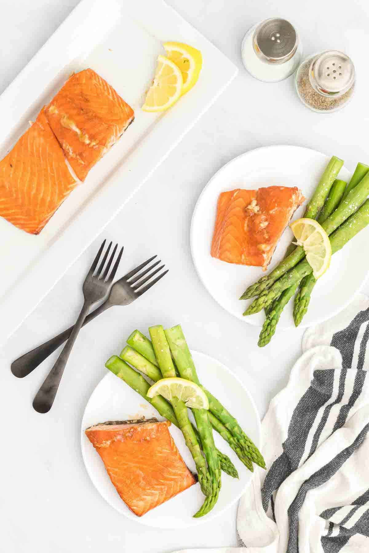 two white plates with the traeger salmon and asparagus and a white platter with extra salmon pieces and lemon wedges.