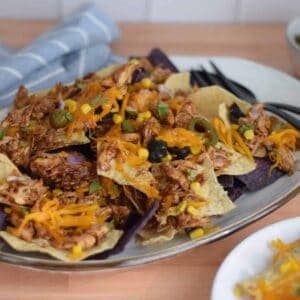 loaded bbq chicken nachos on a white platter with black serving utensils