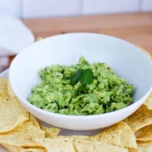 white bowl with homemade guacamole and tortilla chips resting on platter