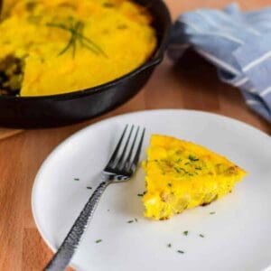 slice of frittata on a white plate with little pieces of garlic chives