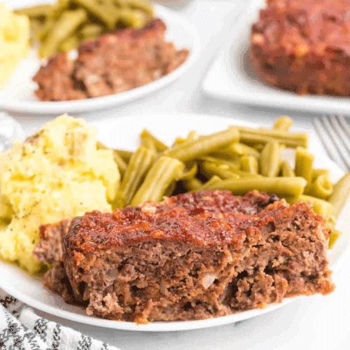 slices of meatloaf on a white plate with mashed potatoes, and green beans