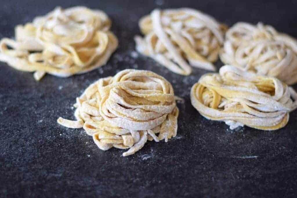 homemade pasta noodles resting into nest piles and drying on black counter top