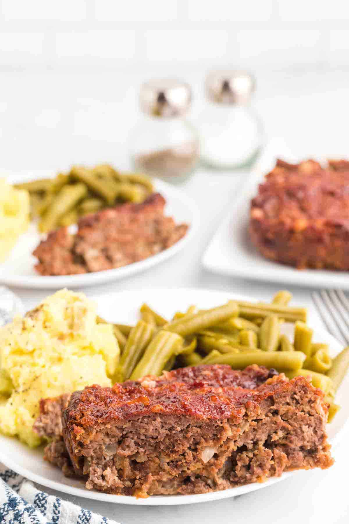 white plates with the smoked meatloaf, mashed potatoes, and green beans