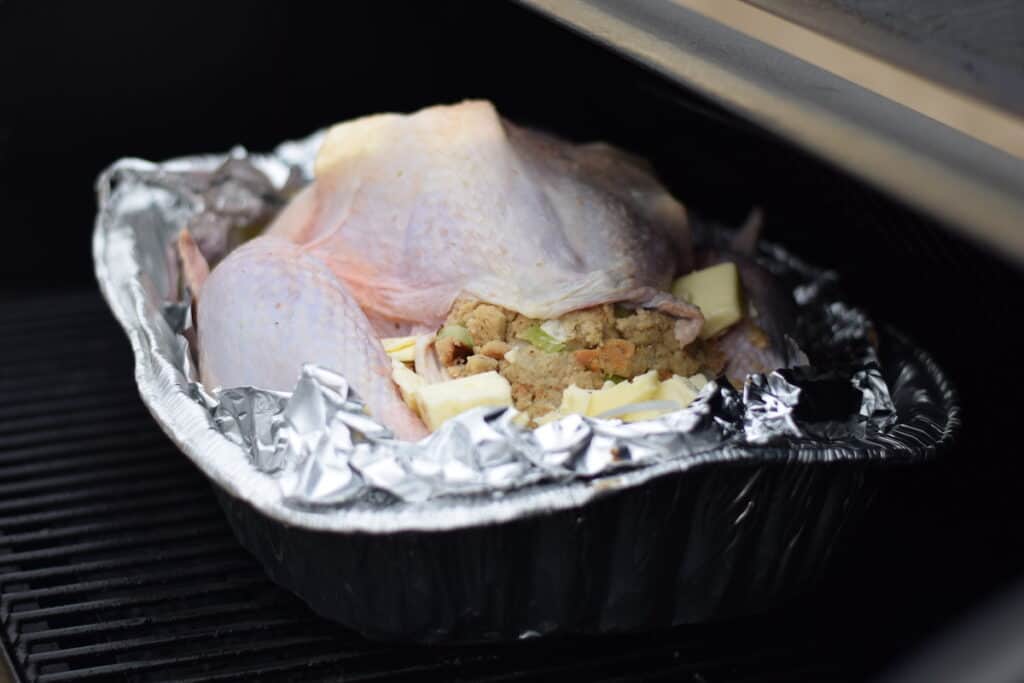 uncooked turkey in a roasting pan and on the traeger grill 