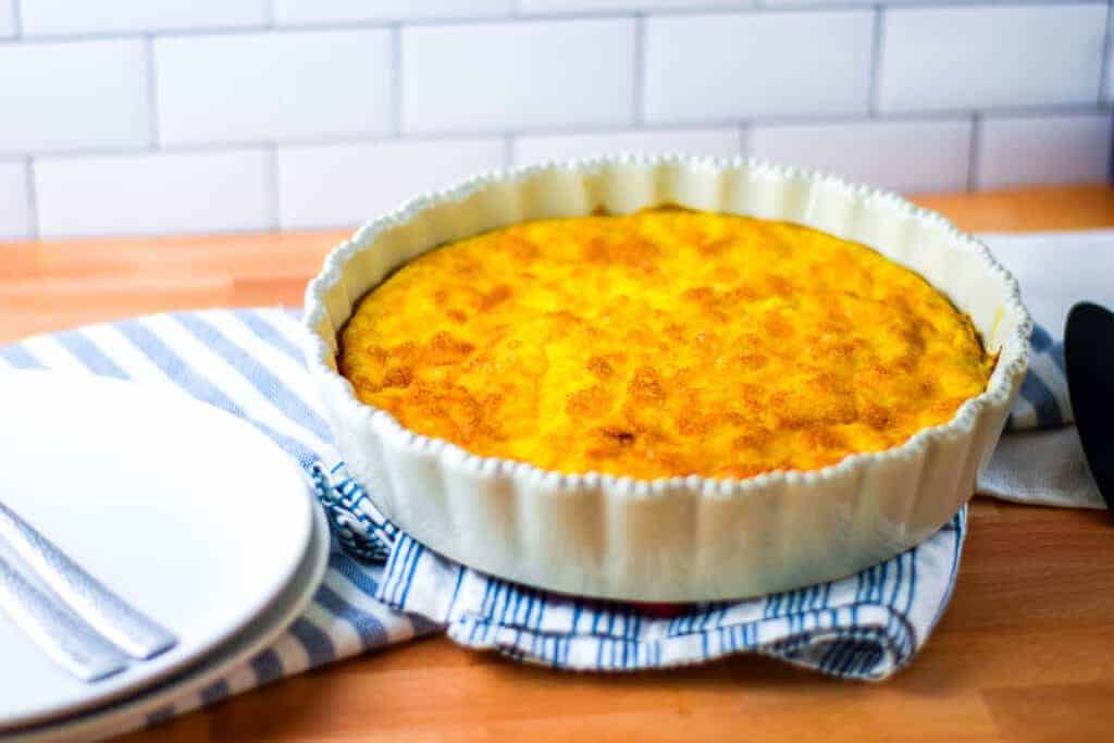 fresh baked caramelized onion quiche with cheddar in a white pie dish and resting on a blue and white tea towel