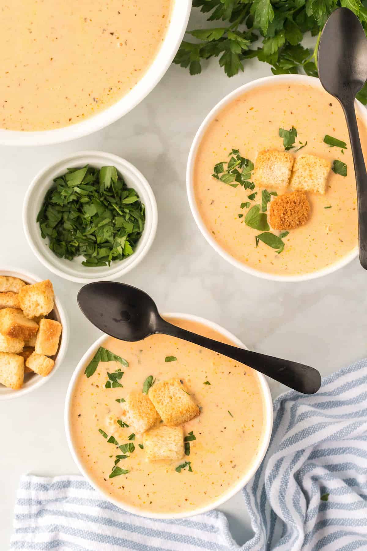 pot of creamy acorn and carrot soup with garnishes of herbs and croutons in bowls