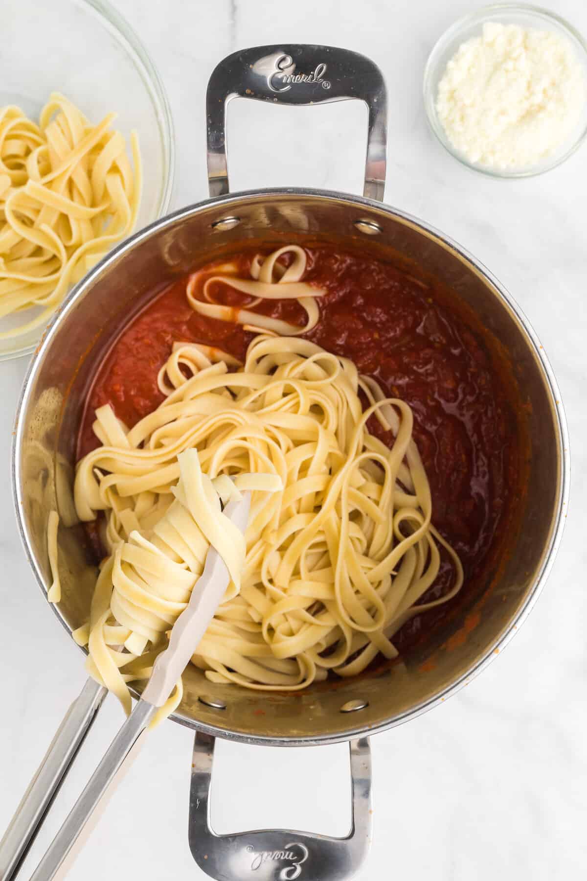adding pasta noodles to the pasta sauce.