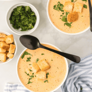 two bowls of creamy acorn and carrot soup with fresh herb garnish and croutons on top