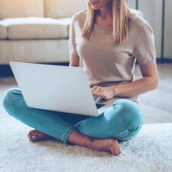 lady with a laptop sitting next to a white couch on the floor