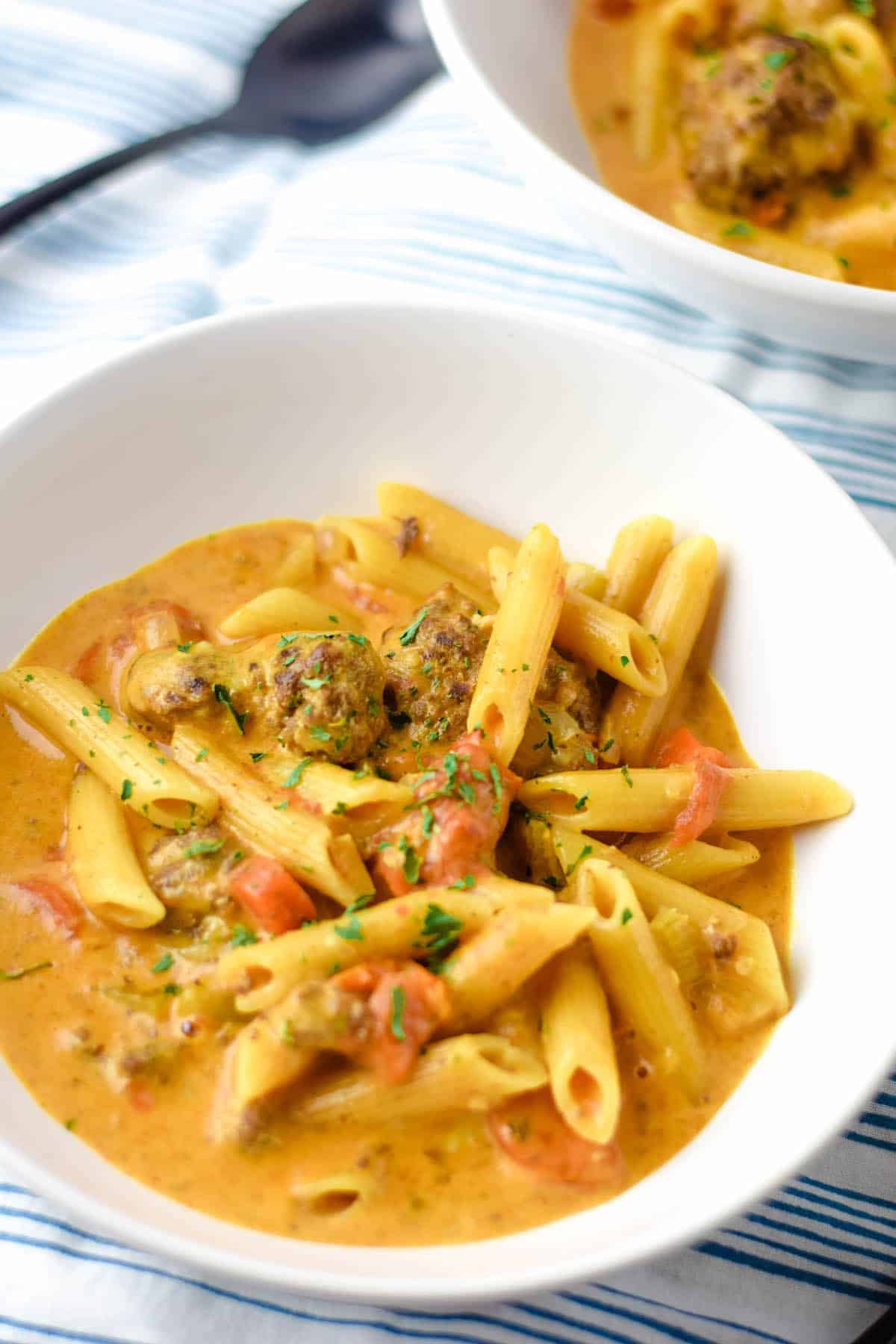 creamy Italian meatball soup in white bowl with a black spoon resting beside it