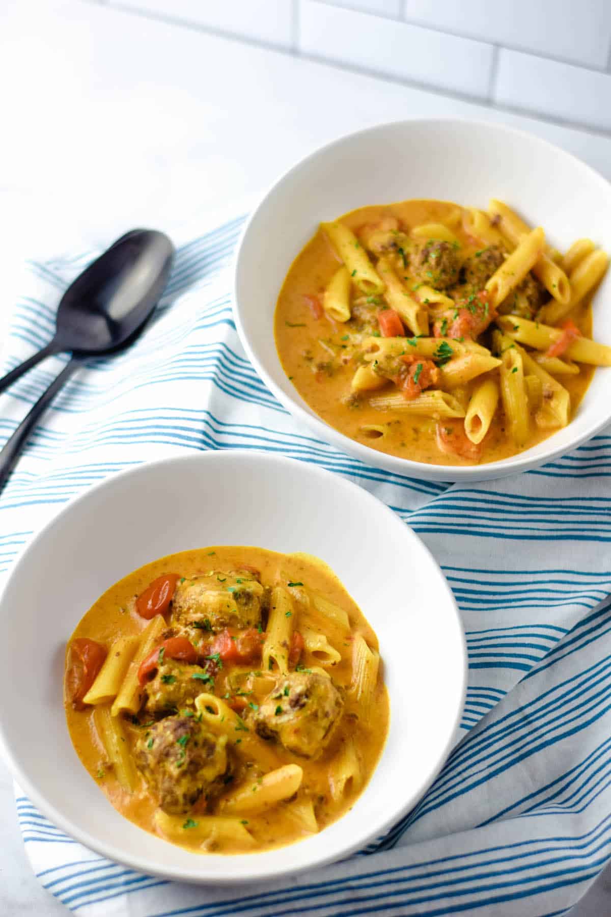 two bowls of meatball soup in white bowls with black spoons resting at the side