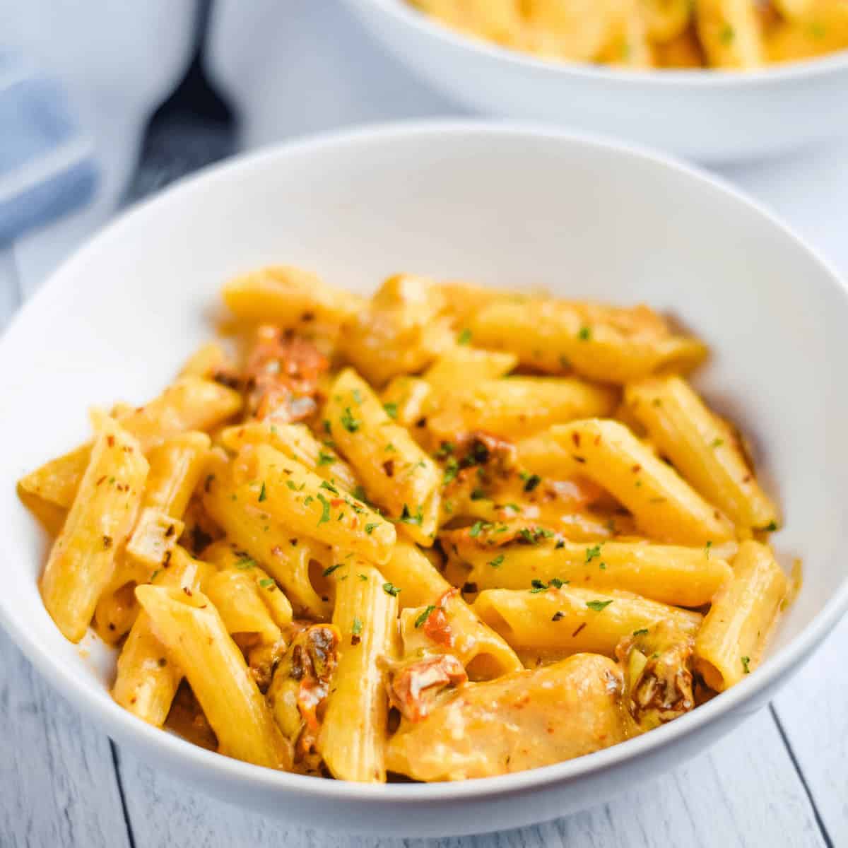 white bowl of finished sun dried tomato pasta with a black fork in background