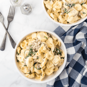 two large white bowls of creamy tortellini with Italian sausage