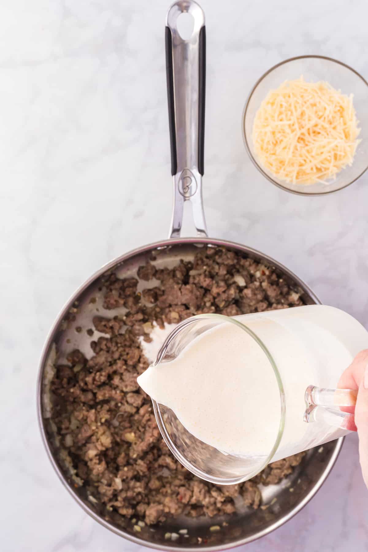 pouring the heavy cream into the skillet with the cooked sausage