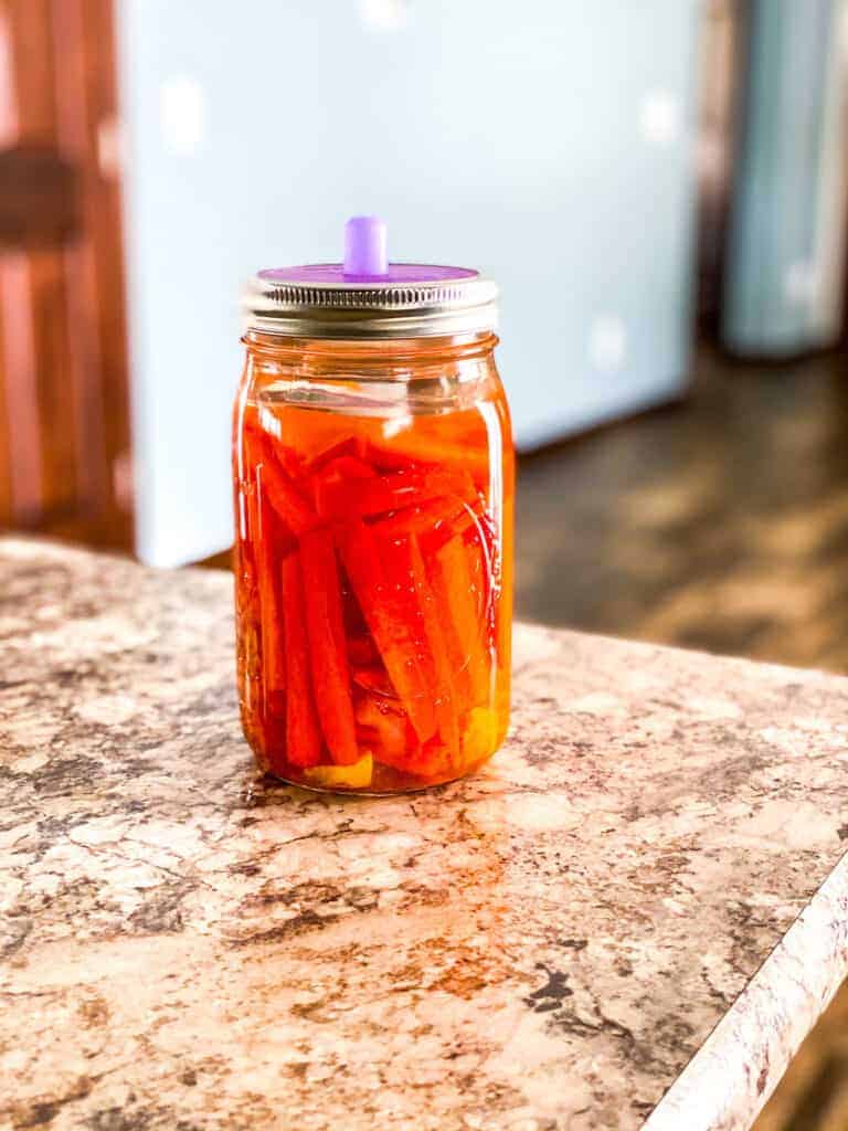 fermented carrots in a mason jar with a purple fermenting lid 