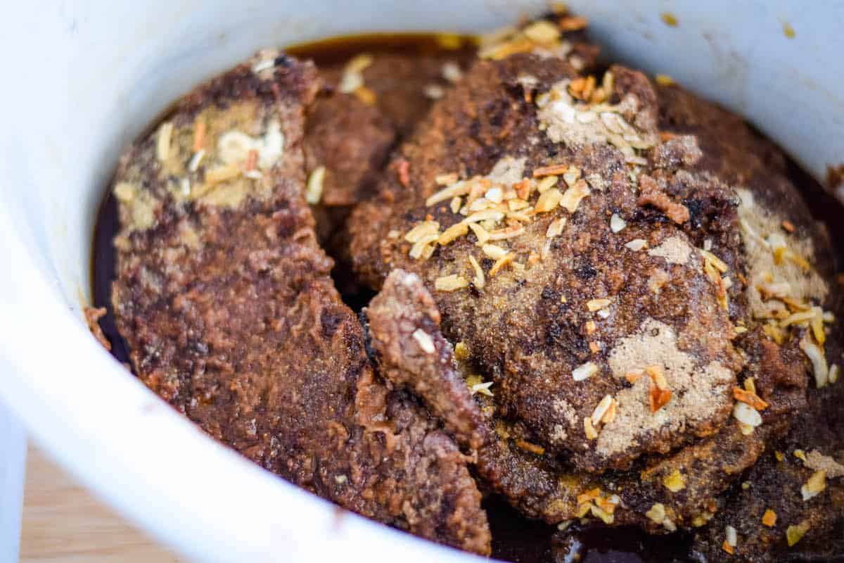 minute steaks with seasonings inside of a crock pot 