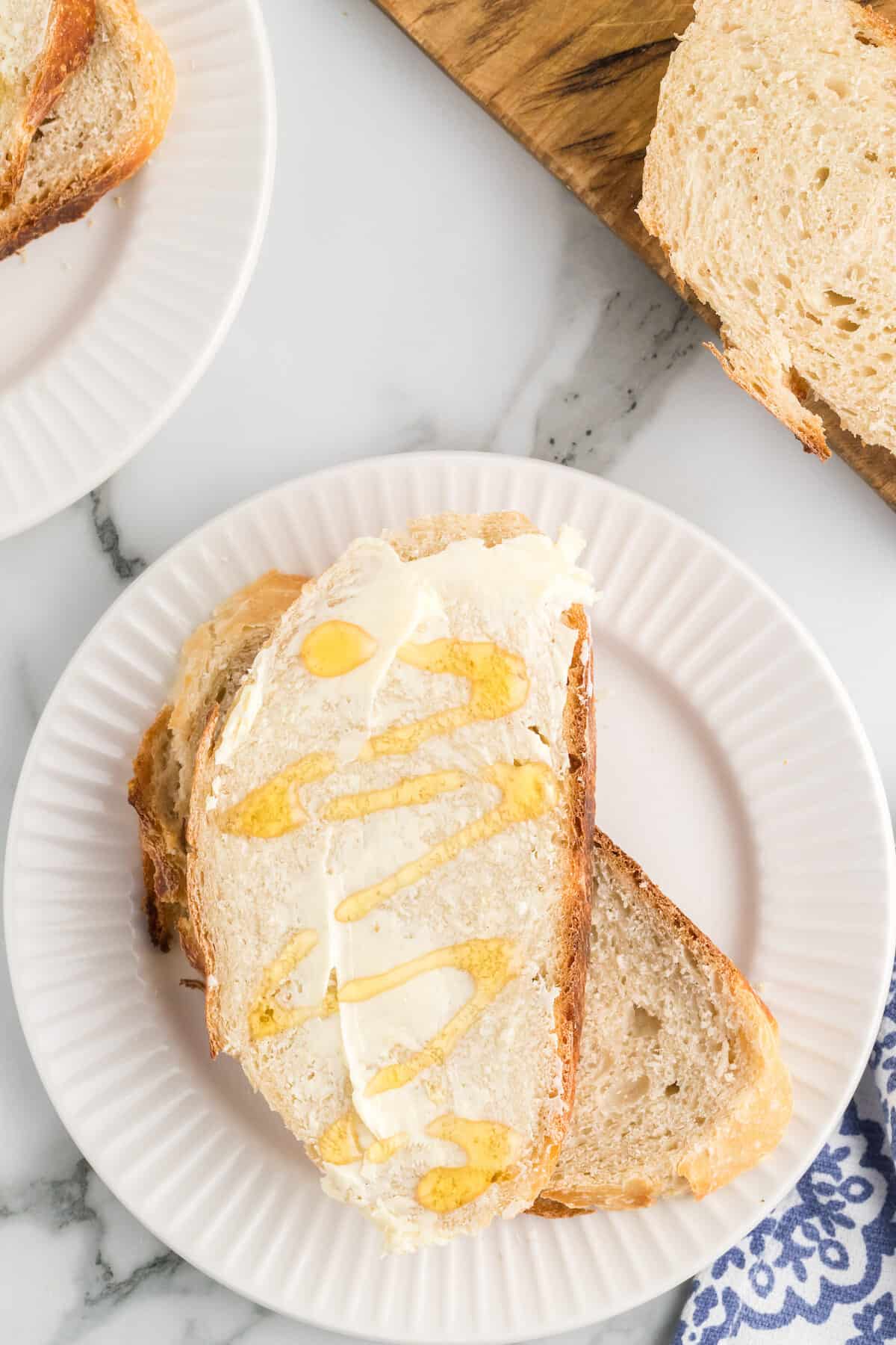slices of artisan bread on a white plate with butter and honey.