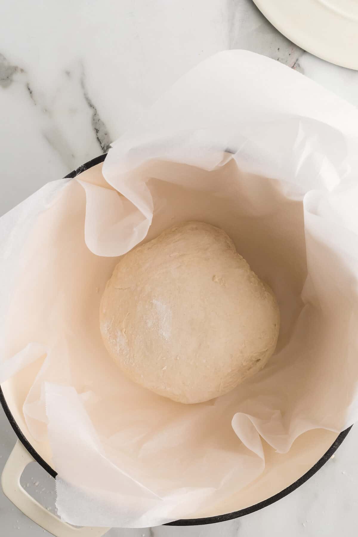 parchment paper lined dutch oven with the artisan loaf inside.