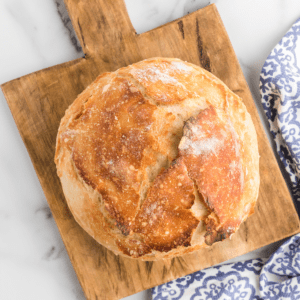 artisan bread loaf on a wooden cutting board with a blue and white tea towel to the side.