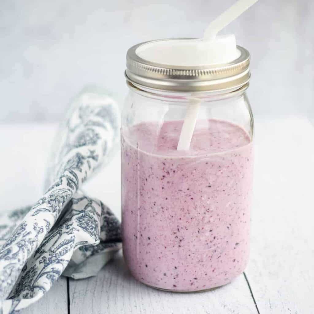 homemade blueberry and banana smoothie in a mason jar with a white straw