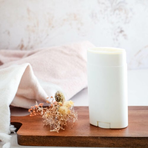 homemade natural deodorant in a white container and standing on a wooden board.