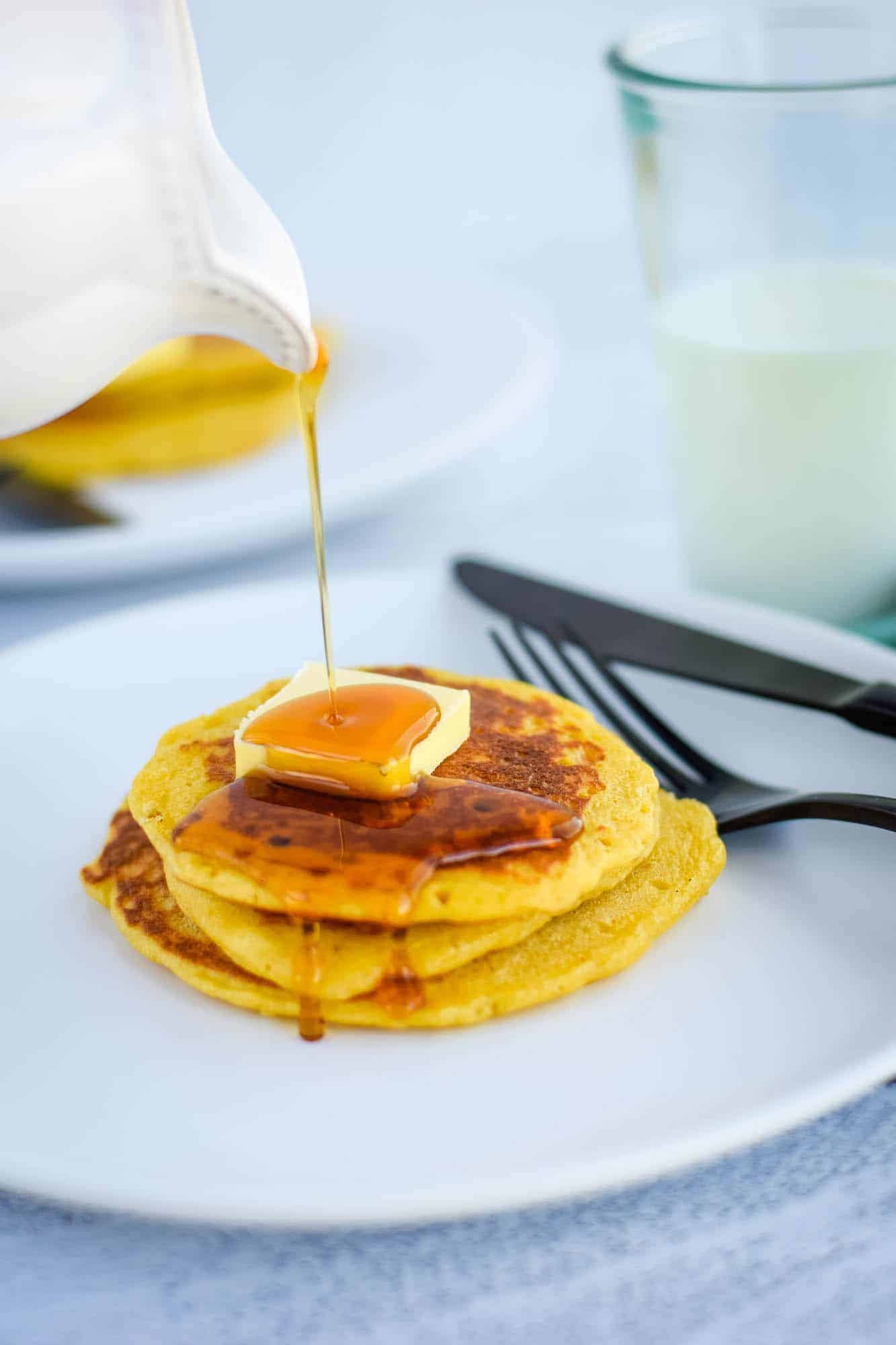pouring maple syrup over a stack of einkorn sourdough pancakes