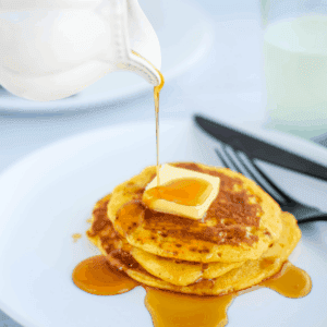 pouring real maple syrup over a stack of cooked einkorn sourdough pancakes