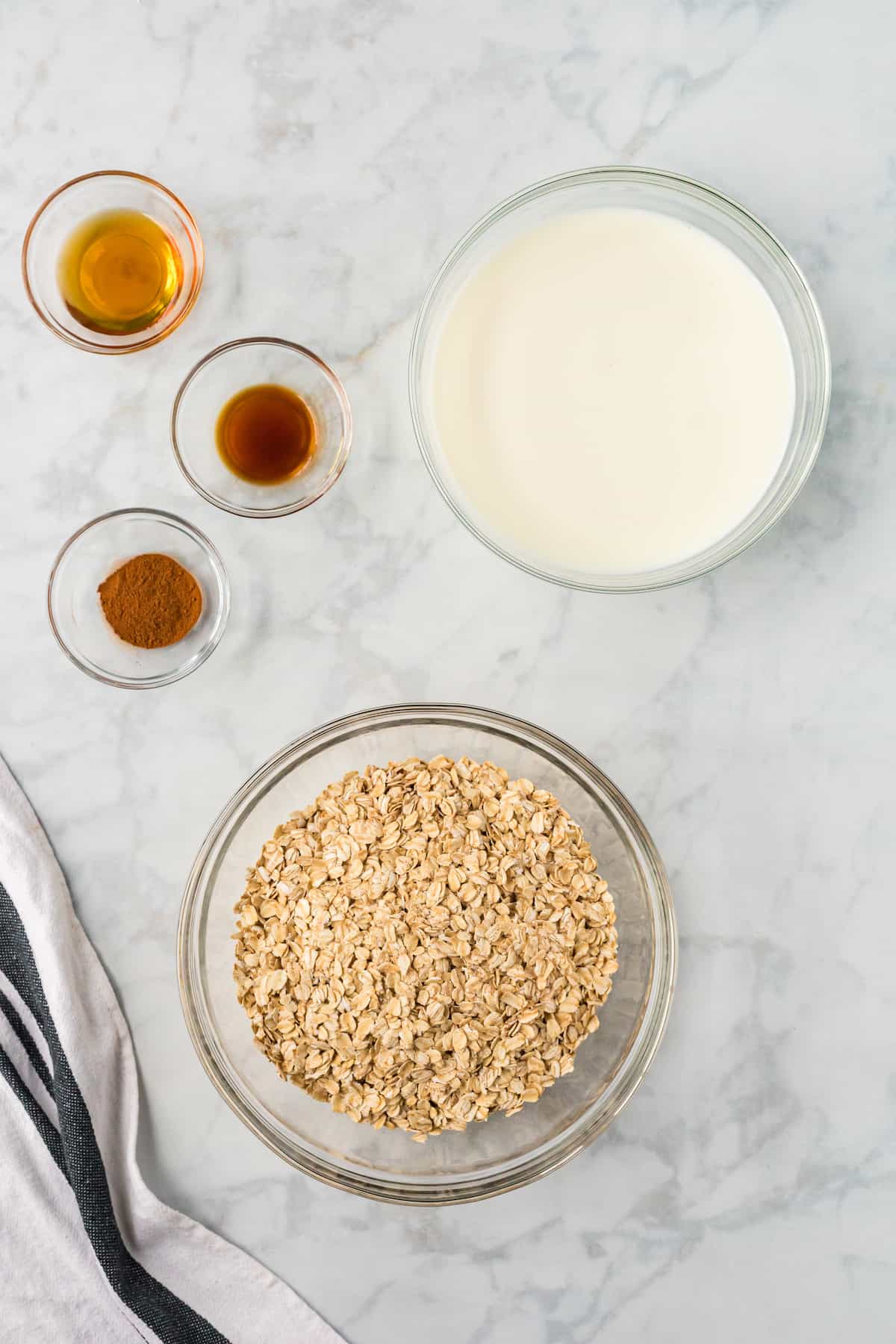 ingredients shot of overnight oats - bowls of oats, milk, cinnamon, vanilla extract, and maple syrup