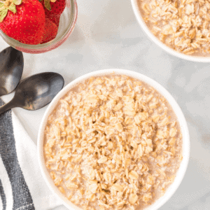 white bowls of overnight oats with jars of fresh strawberries and two black spoons besides the bowls